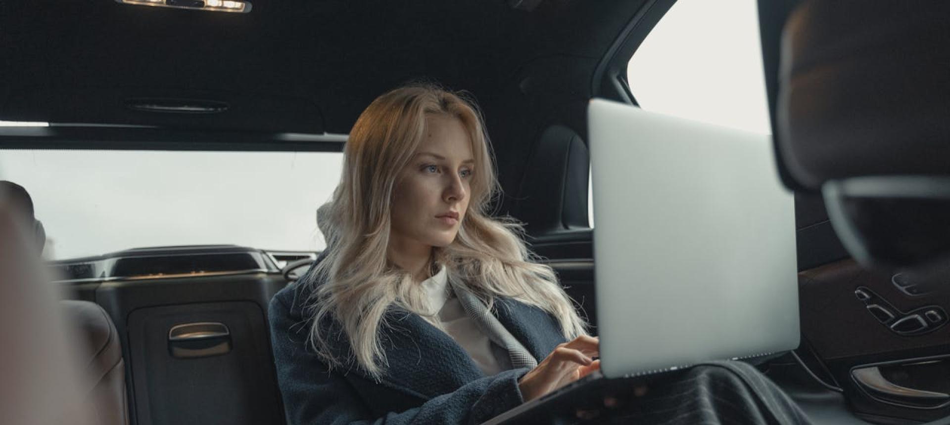 Donna che lavora al laptop seduta sul sedile posteriore di un'auto.