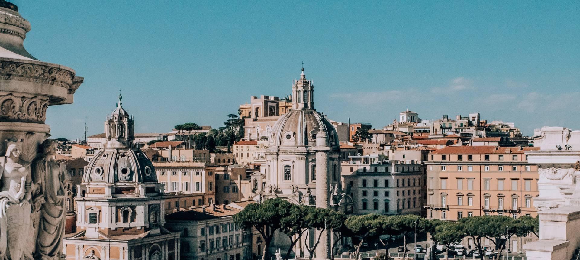 Veduta di Roma con cupole, edifici storici e alberi in un cielo sereno.