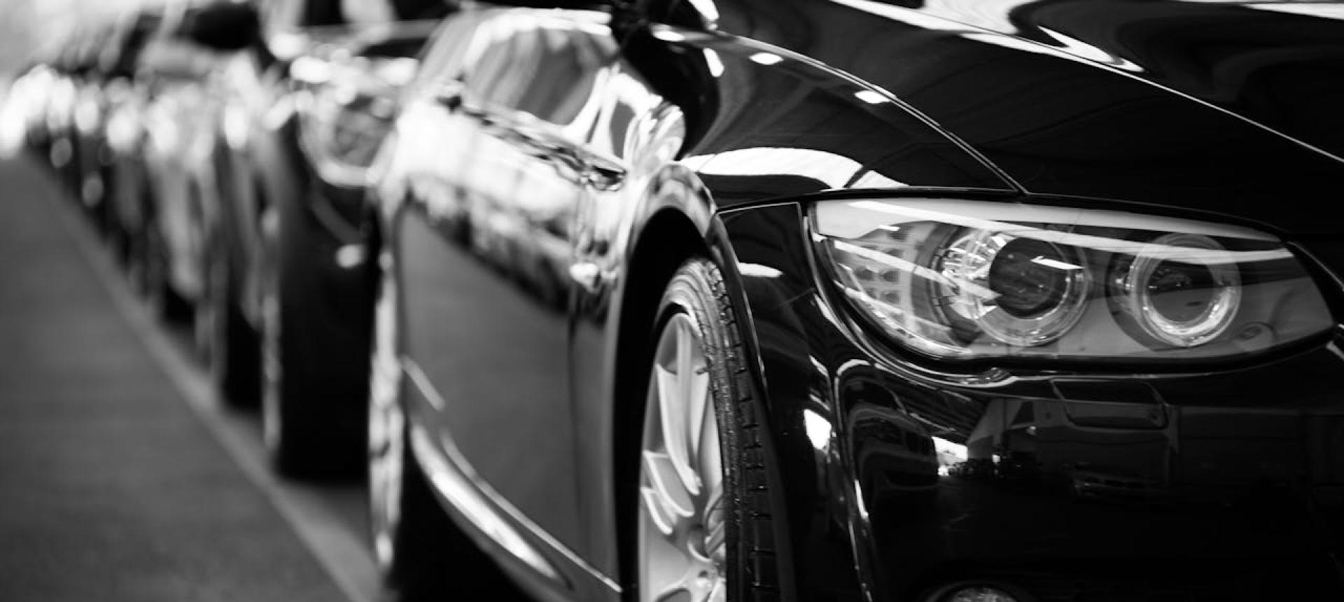 Auto nere in fila, riflessi lucidi, primo piano di un faro.
