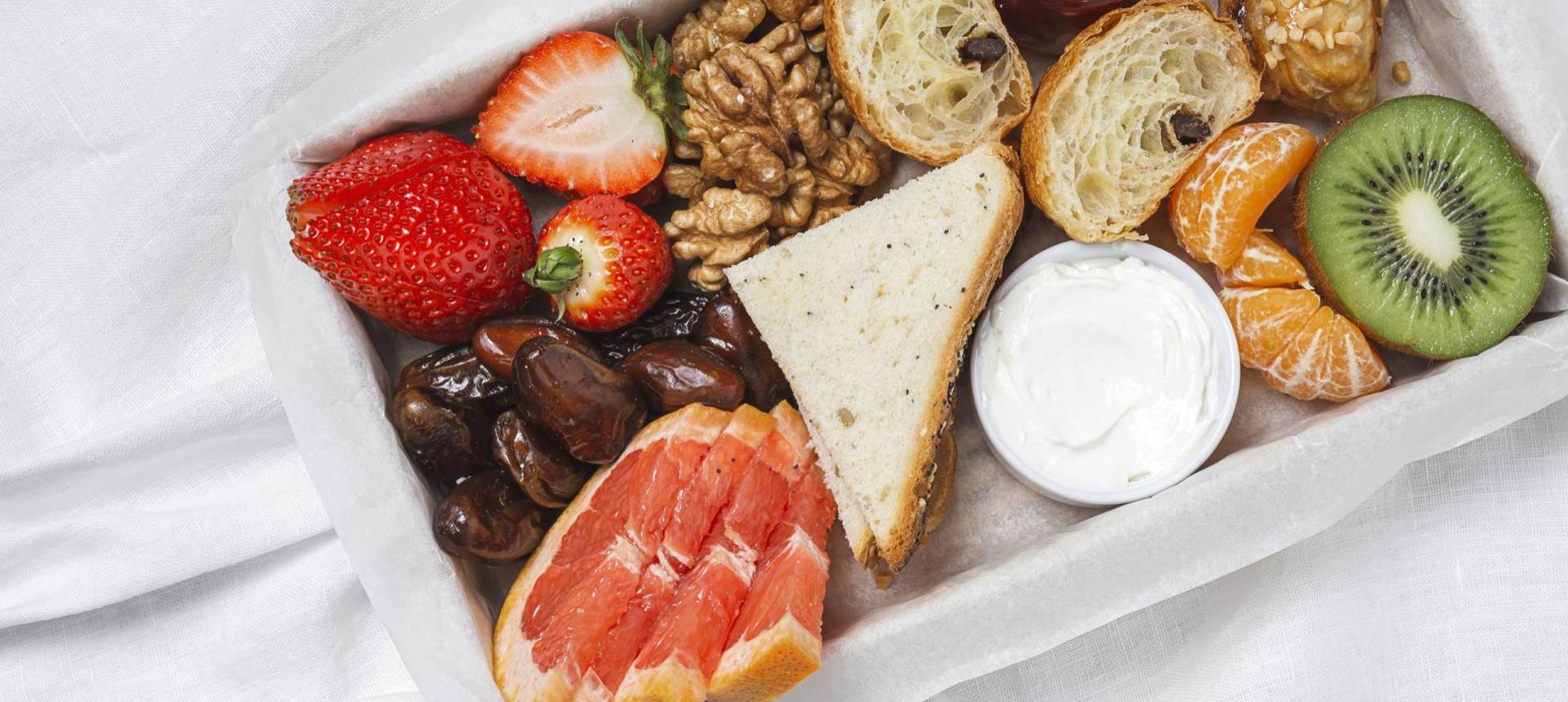 Colazione con frutta, pane, noci e crema su tovaglia bianca.
