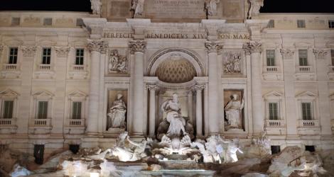 Fontana di Trevi illuminata di notte, con acqua azzurra e statue imponenti.