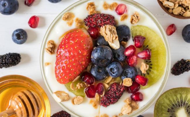 Yogurt con frutta fresca, muesli e miele su tavolo bianco.