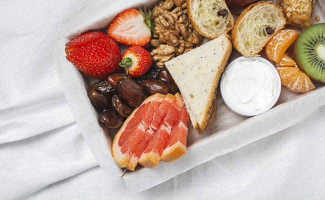 Colazione con frutta, noci, pane, datteri e crema su un vassoio.
