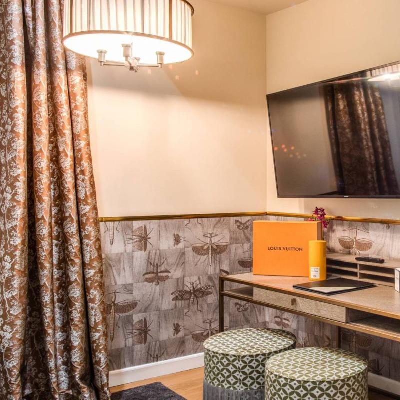 Camera elegante con TV, scrivania e accessori Louis Vuitton, vista su letto ordinato.