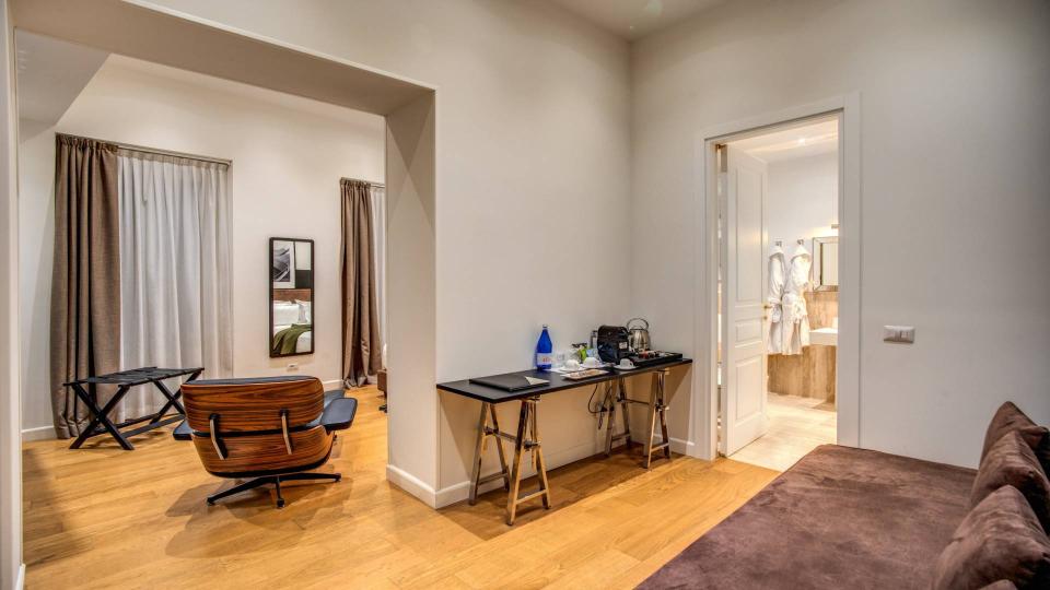 Elegante soggiorno con poltrona, scrivania e accesso al bagno con accappatoi.