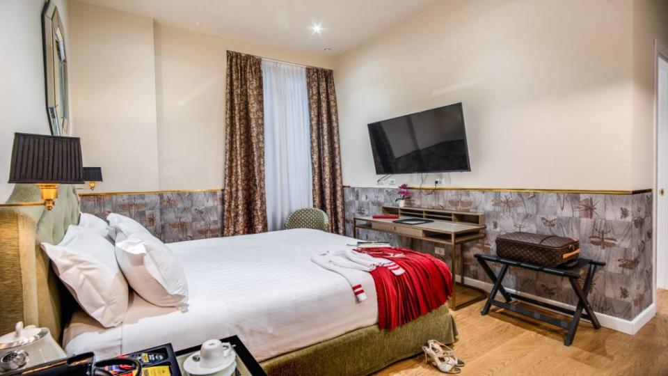 Camera d'hotel elegante con letto matrimoniale, TV a schermo piatto e arredamento raffinato.