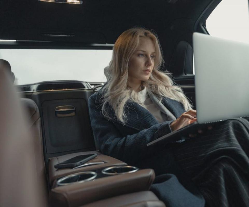 Donna lavora al laptop seduta sul sedile posteriore di un'auto.