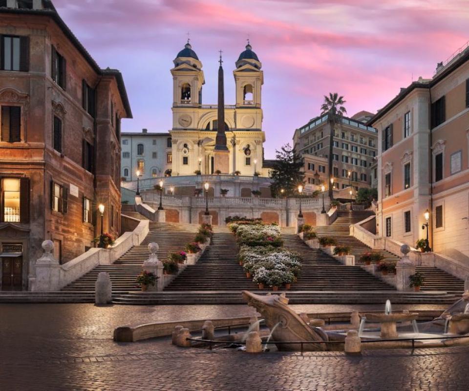 La Scalinata di Trinità dei Monti a Roma, al tramonto, con fontana in primo piano.